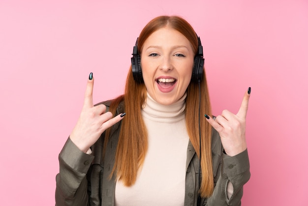 Mujer pelirroja joven escuchando música haciendo gesto de rock