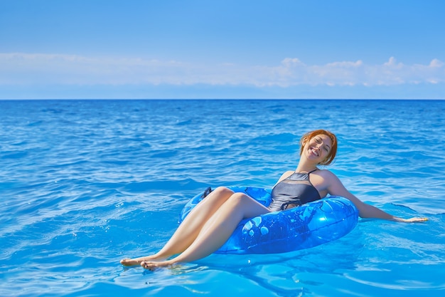 Mujer pelirroja joven flota en el océano en círculo de natación traje de baño de moda negro vacaciones de verano ...