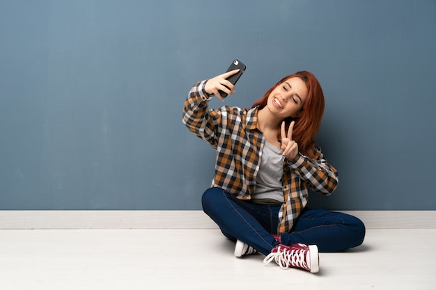 Mujer pelirroja joven sentada en el piso haciendo una selfie