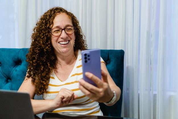 Mujer pelirroja latina de mediana edad en una videollamada en su teléfono celular riendo