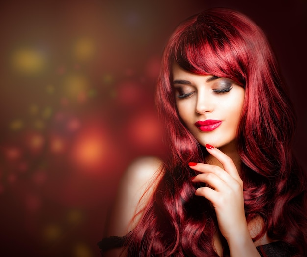 Mujer pelirroja con maquillaje largo peinado rizado rojo y mano cuidada Labios rojos componen un cabello saludable Modelo de moda sobre fondo de brillo nocturno