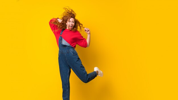 Foto mujer pelirroja con monos saltando sobre pared amarilla aislada