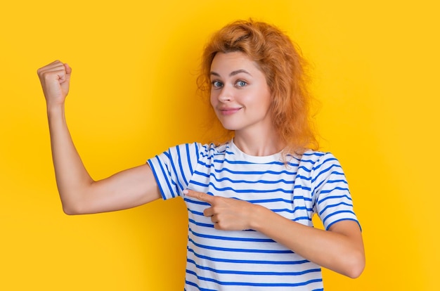 Mujer pelirroja muestra bíceps aislado sobre fondo amarillo retrato de mujer joven pelirroja