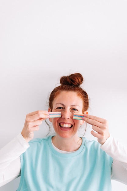 Mujer pelirroja con pecas de caramelo de arco iris en su cara fondo blanco.