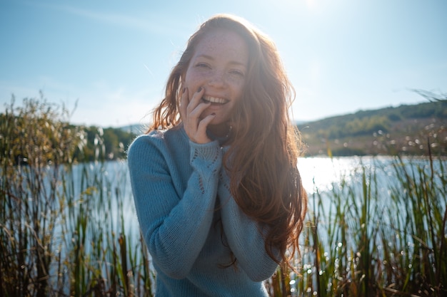 Foto mujer pelirroja en la playa junto al lago en ropa de otoño