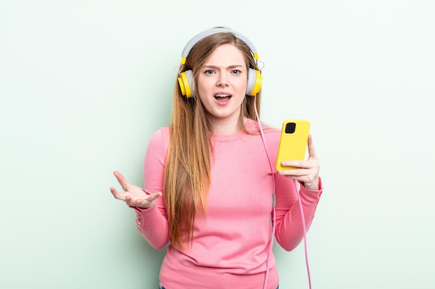 mujer pelirroja que parece enojada, molesta y frustrada. auriculares y concepto de teléfono inteligente