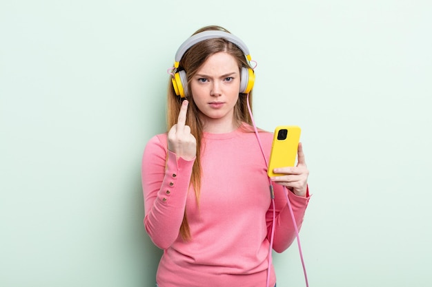 Mujer pelirroja que se siente enojada, molesta, rebelde y agresiva. auriculares y concepto de teléfono inteligente