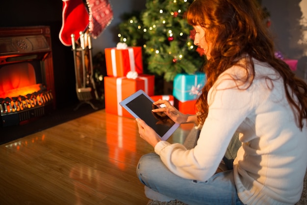 Mujer pelirroja sentada en el piso usando tableta en Navidad