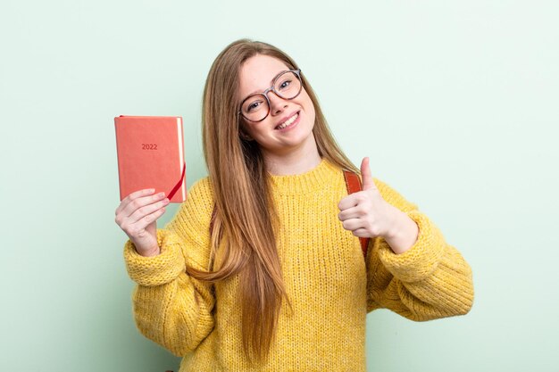 Mujer pelirroja sintiéndose orgullosa, sonriendo positivamente con pulgares arriba concepto de planificador