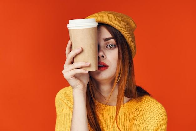 Mujer pelirroja en un sombrero con un suéter con una taza de café estilo de vida fondo rojo