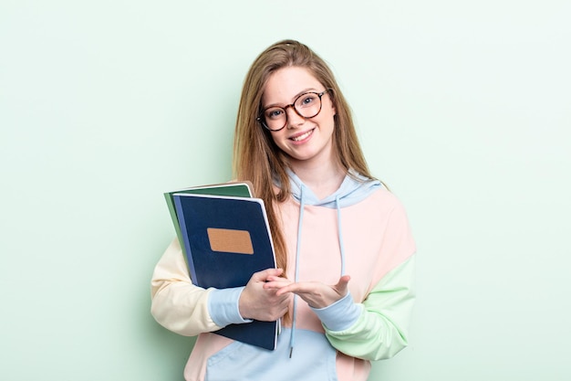 Mujer pelirroja sonriendo alegremente sintiéndose feliz y mostrando un concepto de estudiante