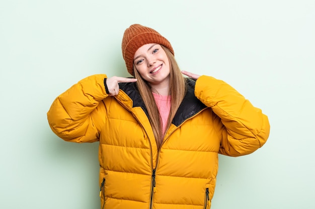 Mujer pelirroja sonriendo con confianza apuntando a su propia amplia sonrisa. concepto de invierno