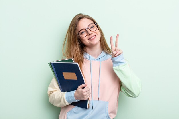 Mujer pelirroja sonriendo y luciendo feliz, gesticulando victoria o paz. concepto de estudiante