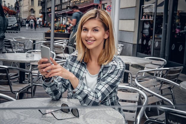 Mujer pelirroja sonriente que usa la aplicación del teléfono inteligente en un café al aire libre.