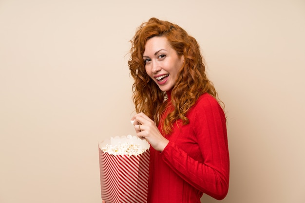 Mujer pelirroja con suéter de cuello alto comiendo palomitas de maíz