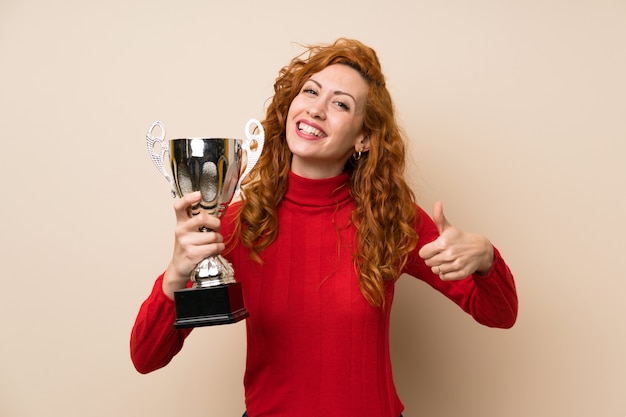 Mujer pelirroja con suéter de cuello alto sosteniendo un trofeo