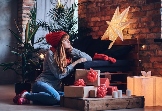 Mujer pelirroja tiene un regalo de Navidad en una sala de estar con interior de loft.