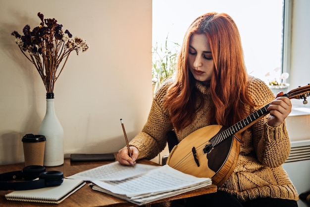 Mujer pelirroja tocando un instrumento musical popular domra acústico y mirando hacia la nota joven