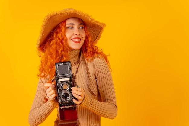Mujer pelirroja turista en un espacio de copia de fondo amarillo con una cámara de fotos vintage