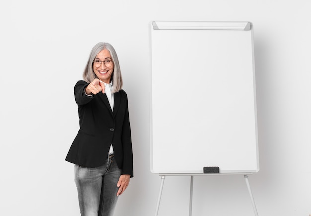 Mujer de pelo blanco de mediana edad apuntando a la cámara eligiéndote y un espacio de copia de tablero. concepto de negocio