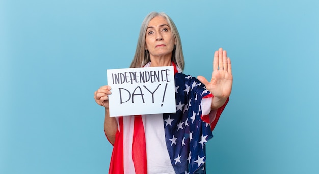 Mujer de pelo blanco de mediana edad mirando seria mostrando la palma abierta haciendo gesto de parada. concepto del día de la independencia