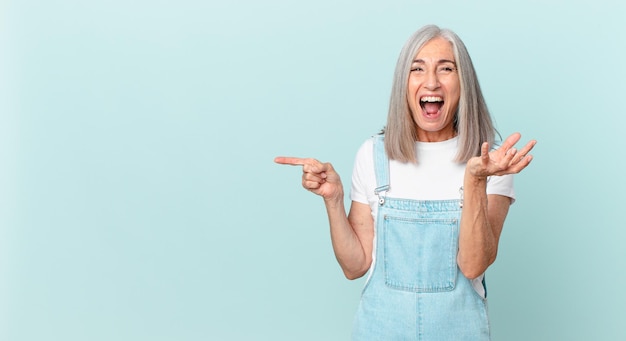 Mujer de pelo blanco de mediana edad que parece enojada, molesta y frustrada y apuntando hacia un lado