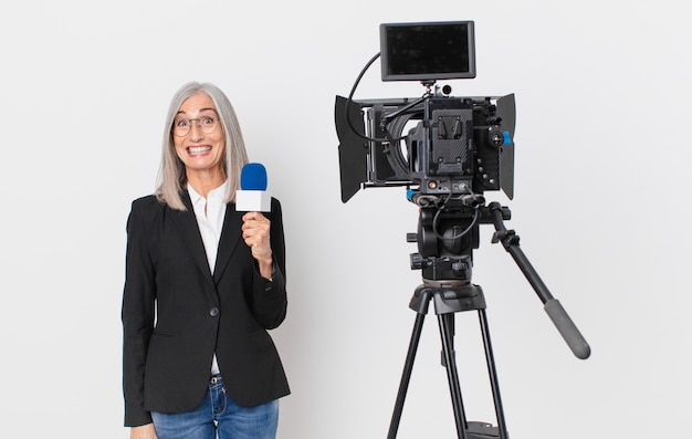 Mujer de pelo blanco de mediana edad que parece feliz y gratamente sorprendida y sosteniendo un micrófono. concepto de presentador de televisión