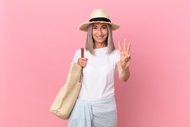 mujer de pelo blanco de mediana edad sonriendo y mirando amigable, mostrando el número tres. concepto de verano