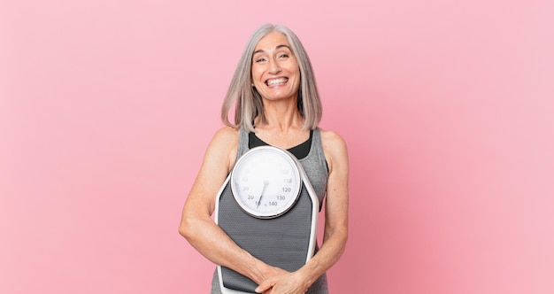 Mujer de pelo blanco de mediana edad sosteniendo un concepto de dieta y fitness de escala de peso