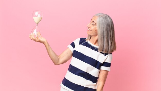 Mujer de pelo blanco de mediana edad sosteniendo un reloj de arena