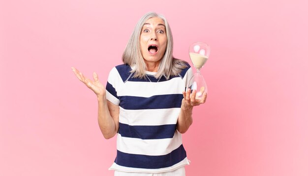 Mujer de pelo blanco de mediana edad sosteniendo un reloj de arena