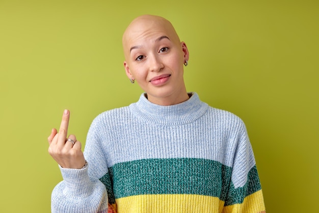 Mujer sin pelo con camisa casual sobre fondo verde aislado mostrando el dedo medio