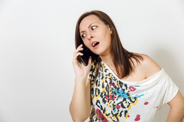 La mujer de pelo castaño enojada hablando por teléfono móvil sobre fondo blanco. Concepto de emociones.