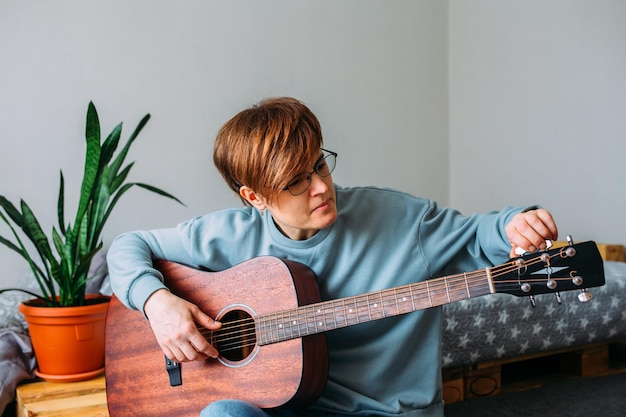 mujer con pelo corto disfruta tocando la guitarra en casa lecciones de música para adultos