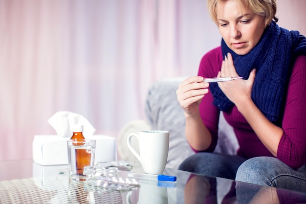 Una mujer con el pelo corto y rubio contrajo gripe y midiendo la temperatura. Concepto de personas, salud y medicina