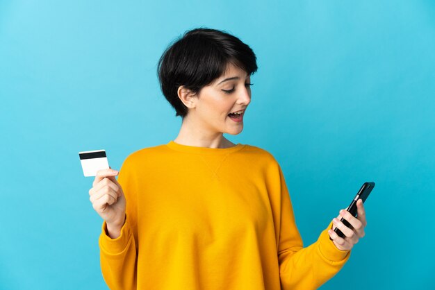 Mujer con pelo corto sobre espacio aislado comprando con el móvil con tarjeta de crédito