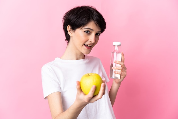 Mujer con pelo corto sobre fondo aislado con una manzana y con una botella de agua