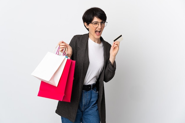 Mujer con pelo corto sobre pared aislada sosteniendo bolsas de compras y una tarjeta de crédito