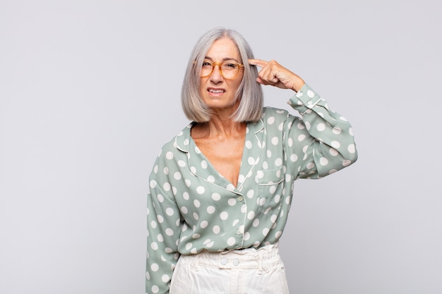 Mujer de pelo gris que se siente confundida y perpleja, mostrando que estás loco, loco o loco