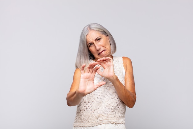 mujer de pelo gris que se siente disgustada y con náuseas, que se aleja de algo desagradable, maloliente o apestoso, diciendo asco