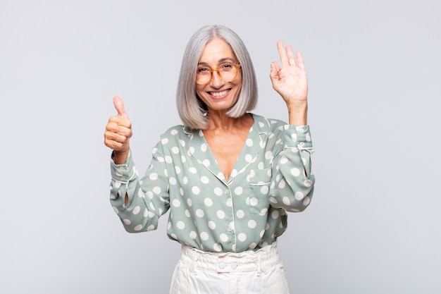 Mujer de pelo gris que se siente feliz, asombrada, satisfecha y sorprendida, mostrando gestos de aprobación y pulgar hacia arriba, sonriendo