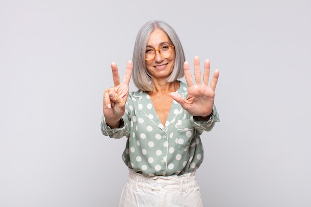 Mujer de pelo gris sonriendo y mirando amistosamente, mostrando el número siete o séptimo con la mano hacia adelante, contando hacia atrás