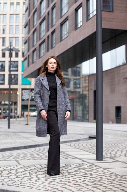 mujer con el pelo largo con un abrigo camina en la ciudad. La mujer está vestida con un abrigo gris y pantalón negro. estilo de vida, streetstyle