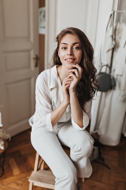 Mujer de pelo largo con camisa blanca mirando a cámara y posando en el apartamento