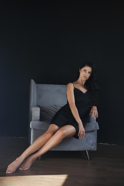 Mujer con el pelo largo y rizado con un vestido negro en casa en un sillón Peinado perfecto