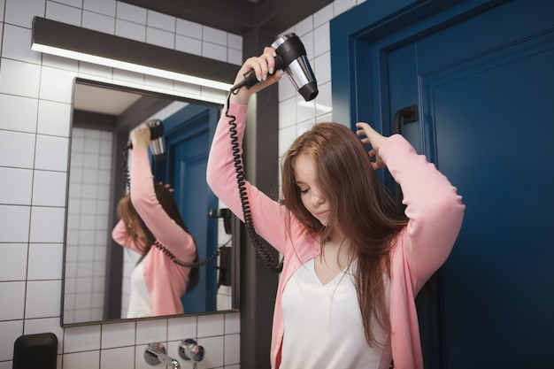 Mujer de pelo largo con secador de pelo en el baño de la habitación del hotel