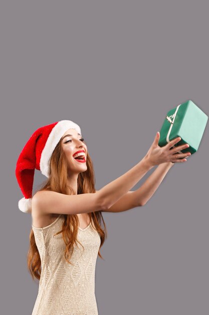 Foto mujer de pelo largo con sombrero rojo de santa claus con labios rojos atrapando una caja de regalo