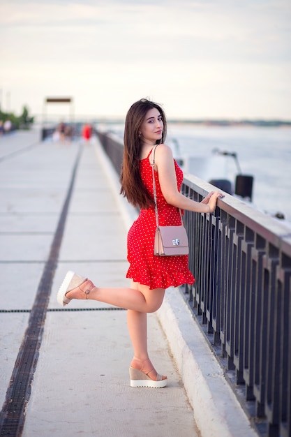 Una mujer con el pelo largo con un vestido rojo de verano camina por el terraplén