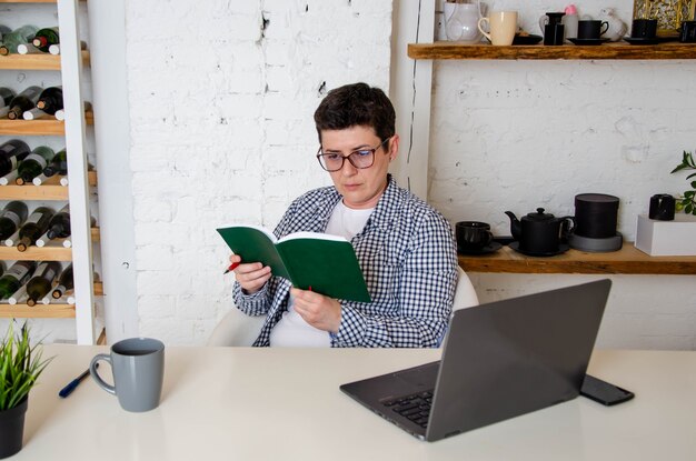 Mujer con pelo negro corto con gafas se sienta atentamente a la mesa, tomando notas en el cuaderno. Planificación, elaboración de presupuestos.