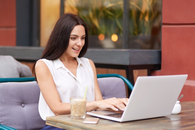 Mujer de pelo oscura positiva en tipos de ropa elegante en la computadora portátil